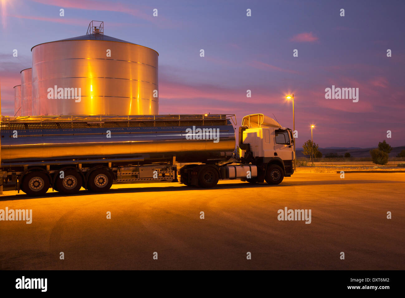 Stainless steel milk tanker parked next to silage storage tower at night Stock Photo