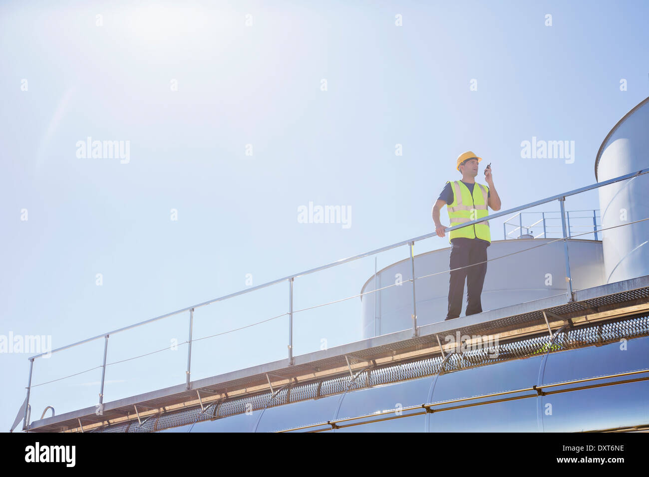 Worker using walkie-talkie on platform next to silage storage towers Stock Photo