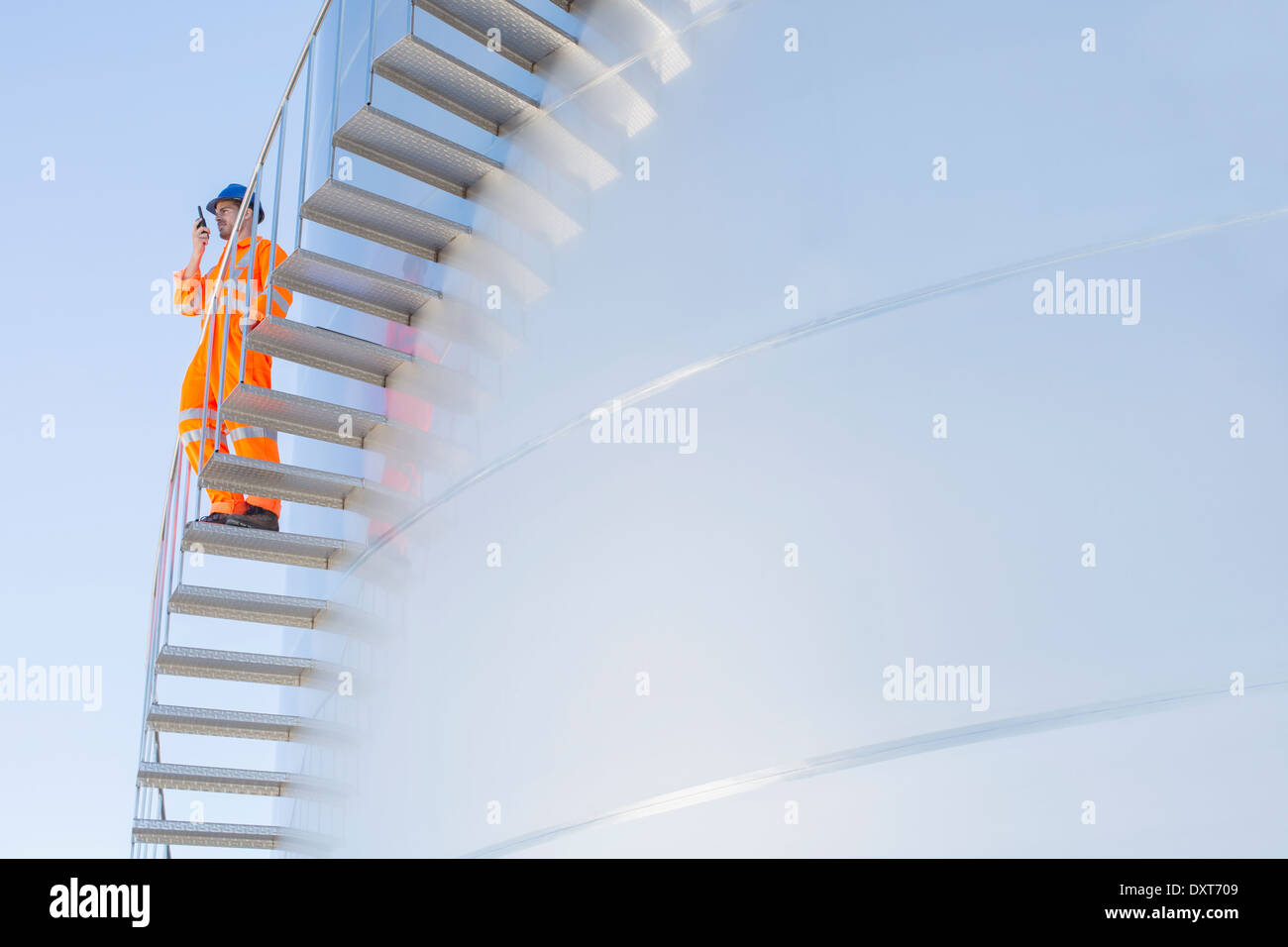 Worker using walkie-talkie on stairs along silage storage tower Stock Photo