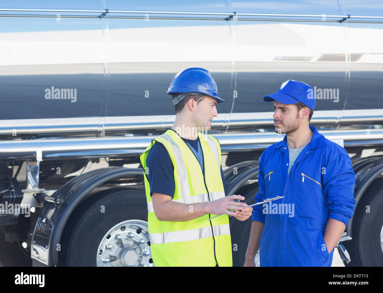 Workers with clipboard talking next to stainless steel milk tanker Stock Photo