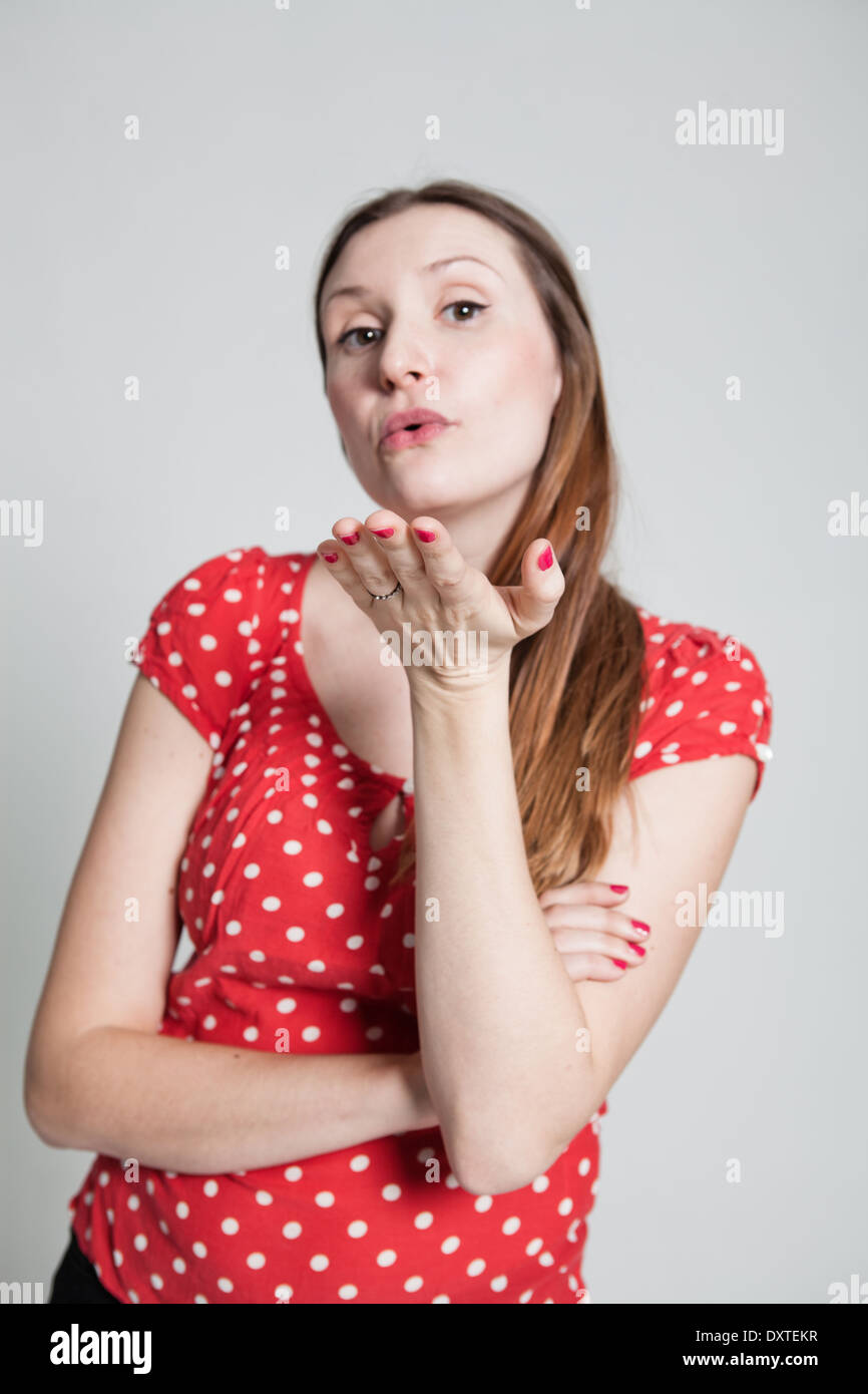 Studio portrait of attractive woman wearing spotty red blouse with pursed lips blowing a kiss Stock Photo