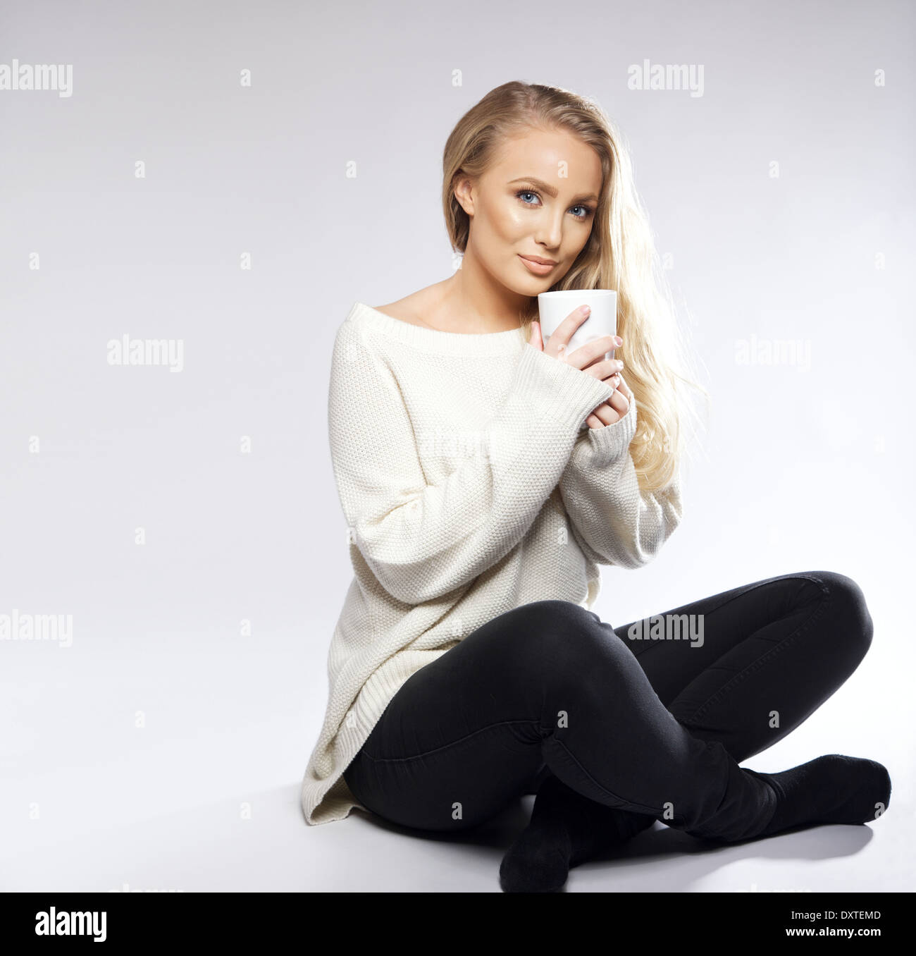 Young woman sitting on floor with cup of coffee or tea. Isolated shot ...