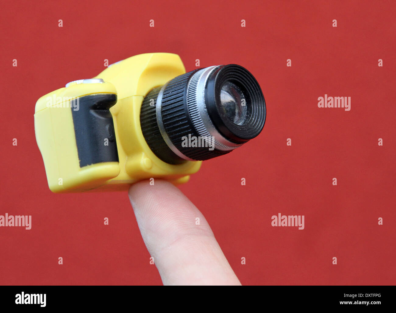 index finger holding a small yellow suspended camera and red background Stock Photo