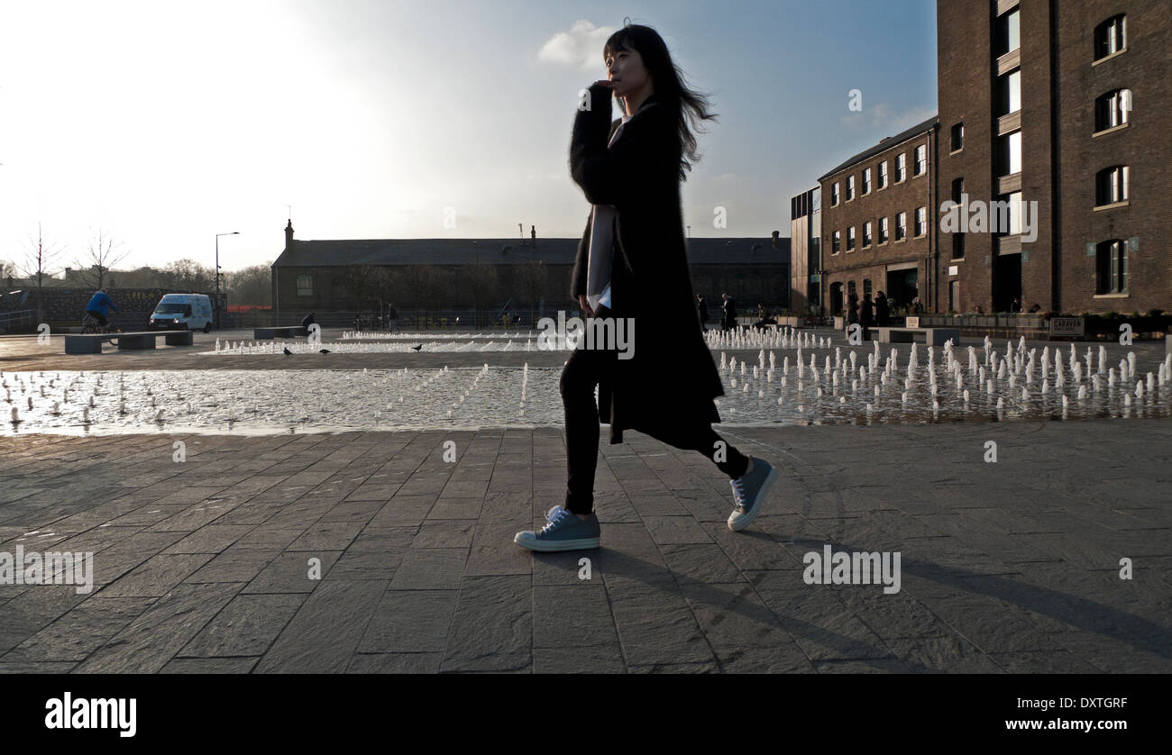 Young Asian woman walking past fountain at UAL University of the Arts CSM Central St Martins,  Kings Cross London N1  KATHY DEWITT Stock Photo