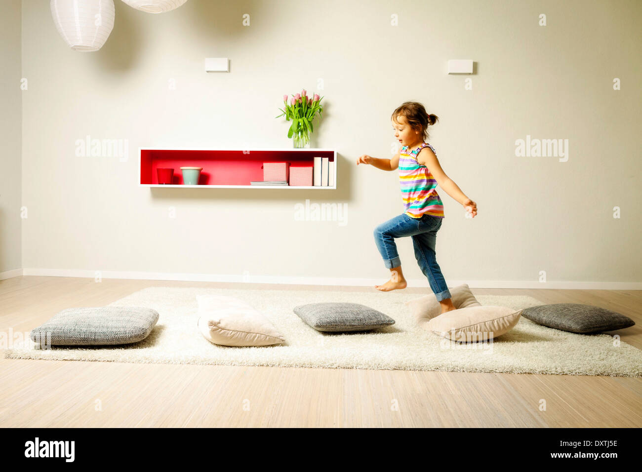 Girl in living room walking across cushions, Munich, Bavaria, Germany Stock Photo