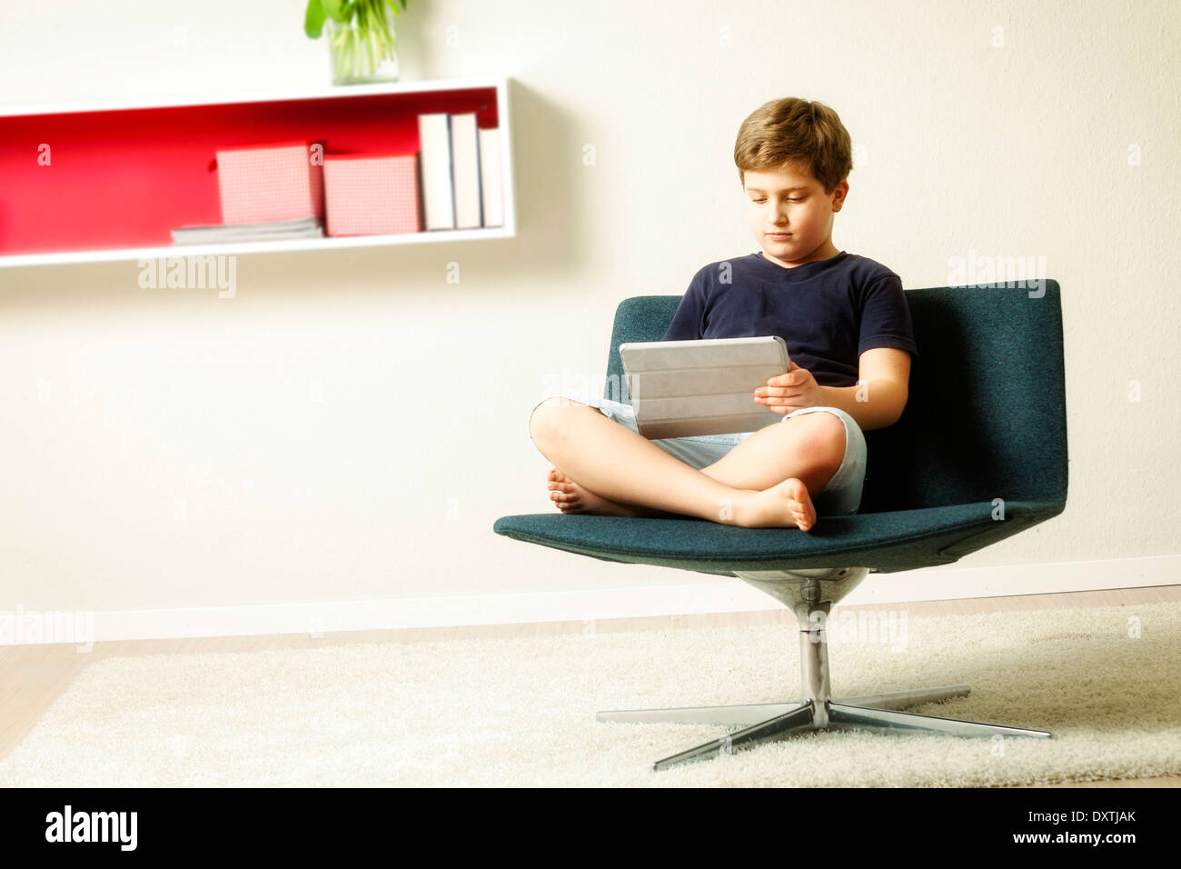 Boy sits in chair using tablet computer, Munich, Bavaria, Germany Stock Photo