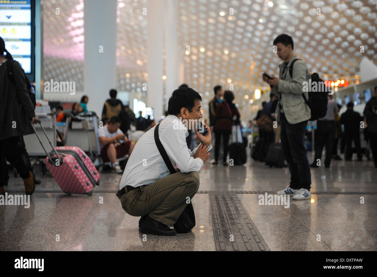 Shenzhen, China's Guangdong Province. 31st Mar, 2014. Stranded passengers make phone calls while waiting at the airport of Shenzhen, south China's Guangdong Province, March 31, 2014. Heavy rain also grounded flights and stranded passengers at major airports of Guangdong since Sunday. As of 6:30 p.m., a total of 113 flights had been canceled at the Shenzhen Bao'an International Airport on Monday, with 43 outbound flights delayed for at least two hours, according to sources with the airport. © Mao Siqian/Xinhua/Alamy Live News Stock Photo