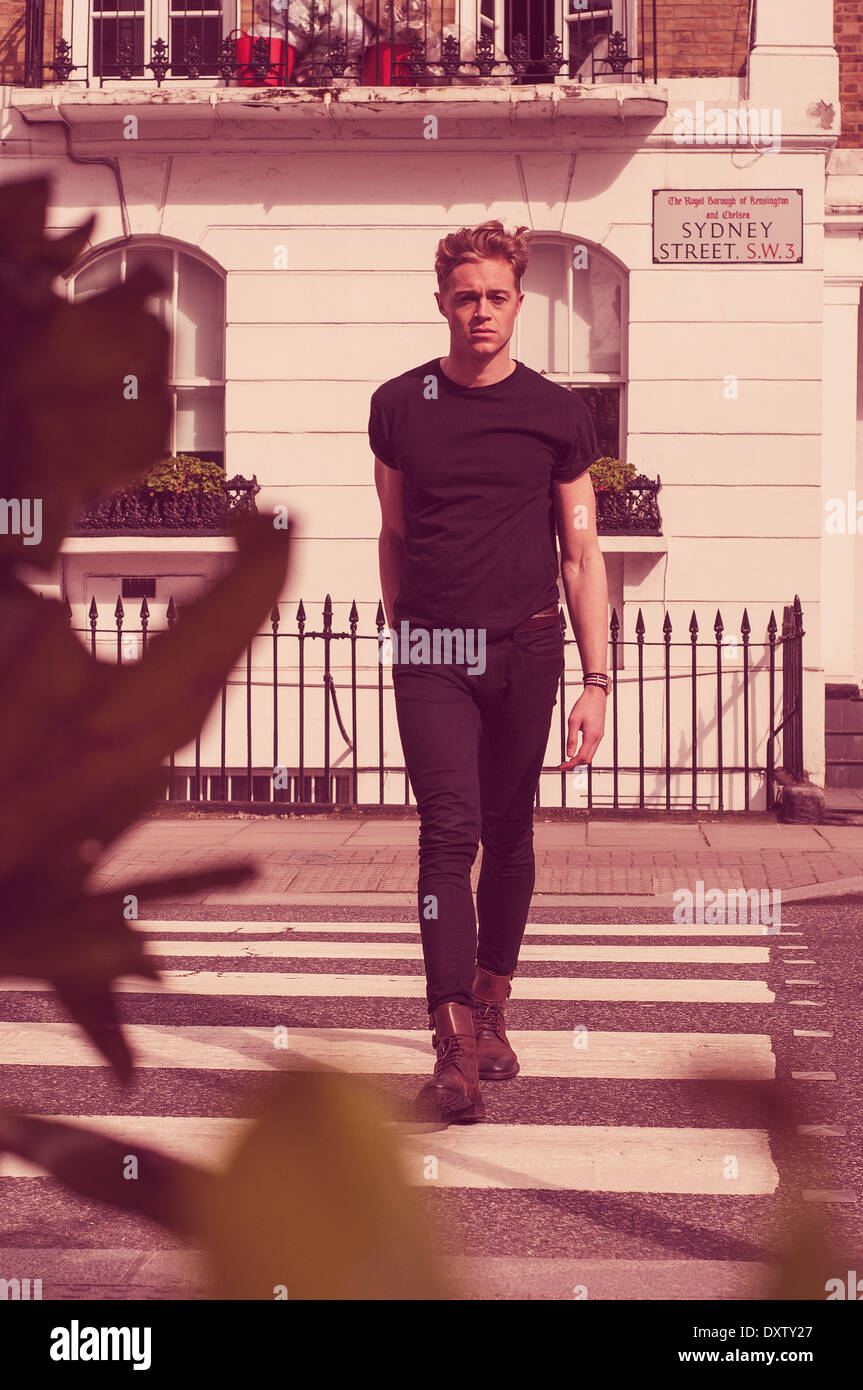 Male model dressed in black walking across London street Stock Photo