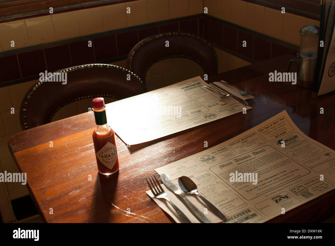 Diner condiments sit on the table in a small town diner.  Place mats advertise local businesses. Stock Photo