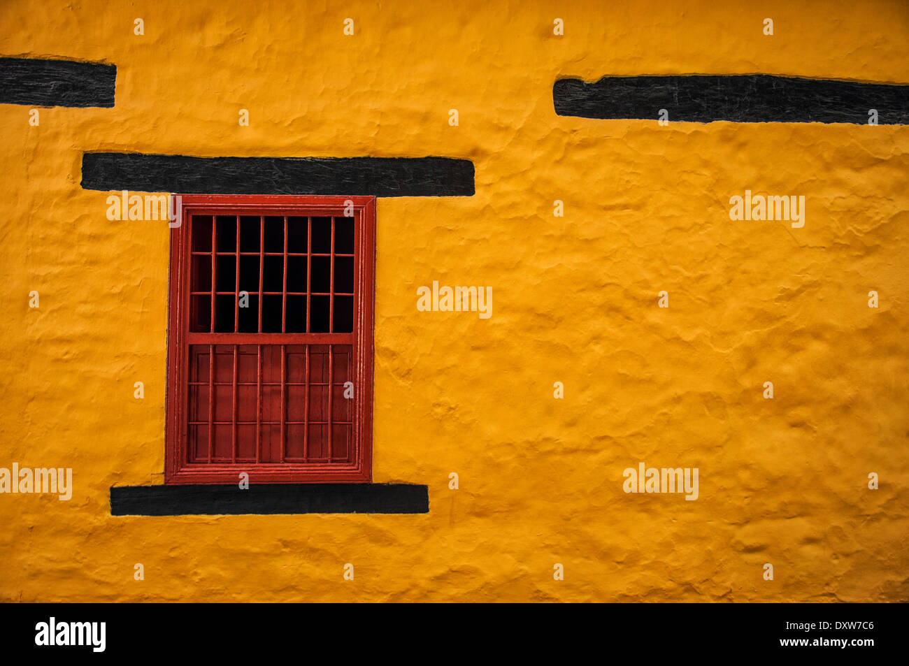 A yellow colonial wall with a red window. Stock Photo