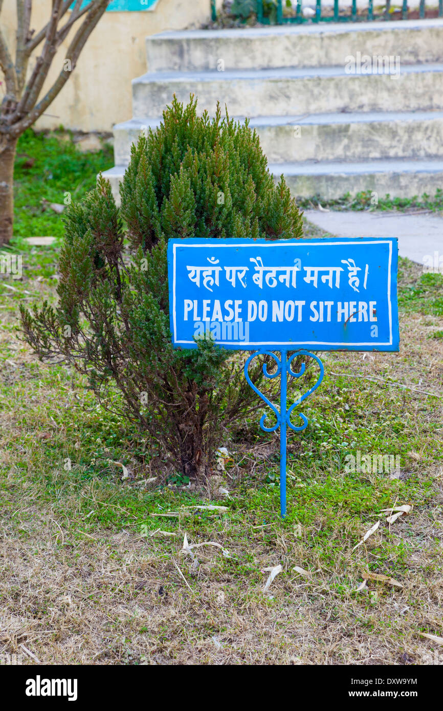 India, Dehradun. Bilingual Sign Prohibiting Sitting on Grass on Grounds of Buddhist Temple of Dehradun at Mindrolling Monastery. Stock Photo