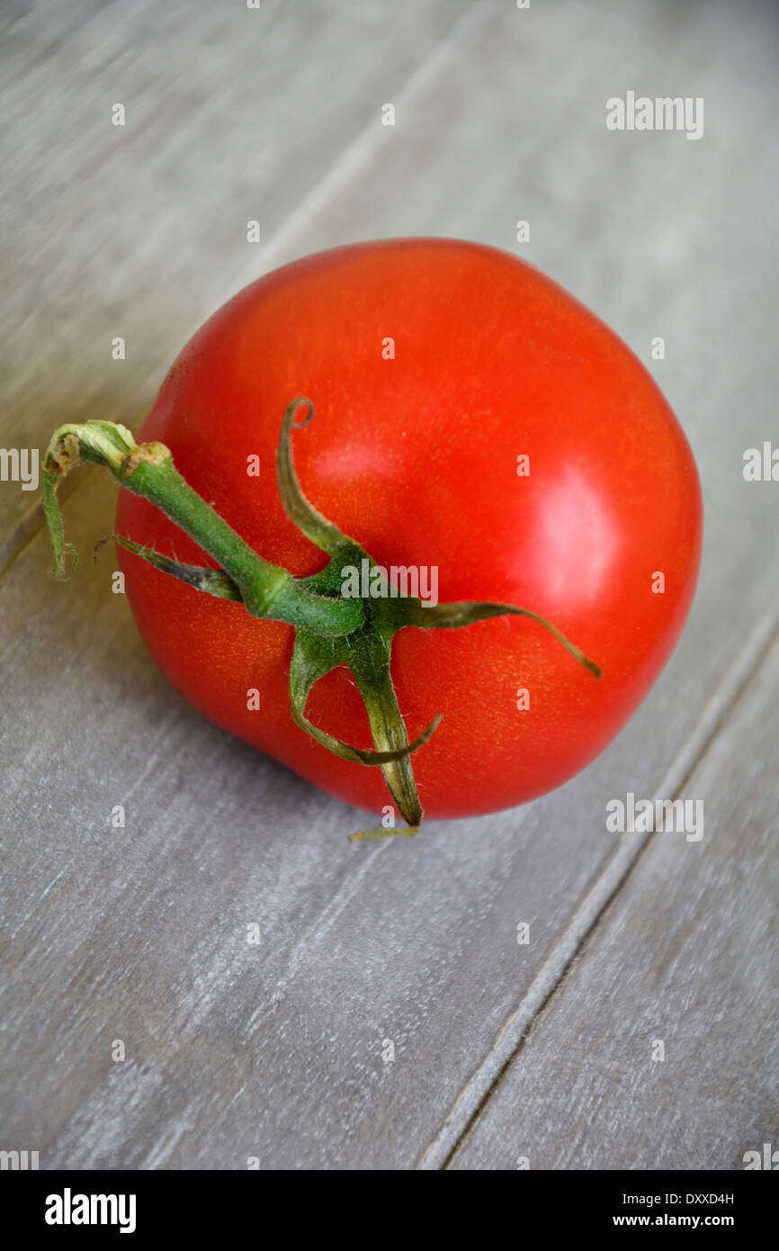 One fresh red tomato on a wooden table macro close-up Eine ganze rote frische Tomate mit Blattgrün auf einem Holztisch Stock Photo