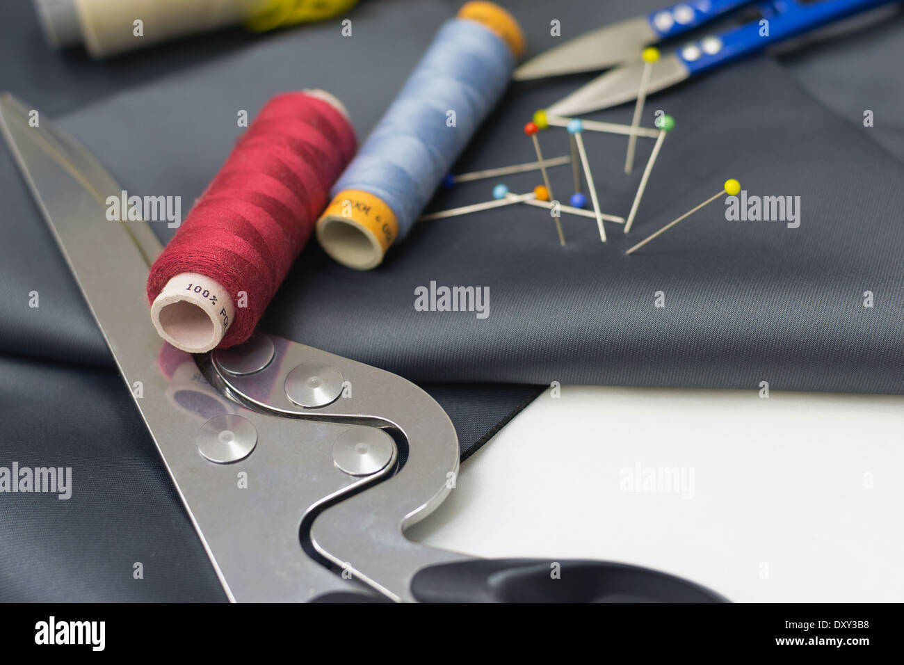 Thread spools, pin and yellow measuring tape on grey fabric. Stock Photo