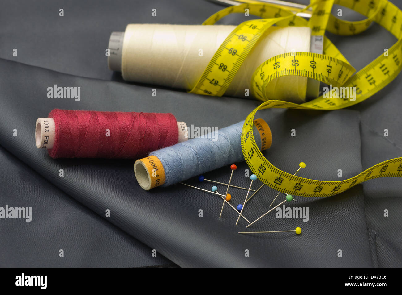 Tailors tools - thread spools, pin and yellow measuring tape on grey fabric. Stock Photo