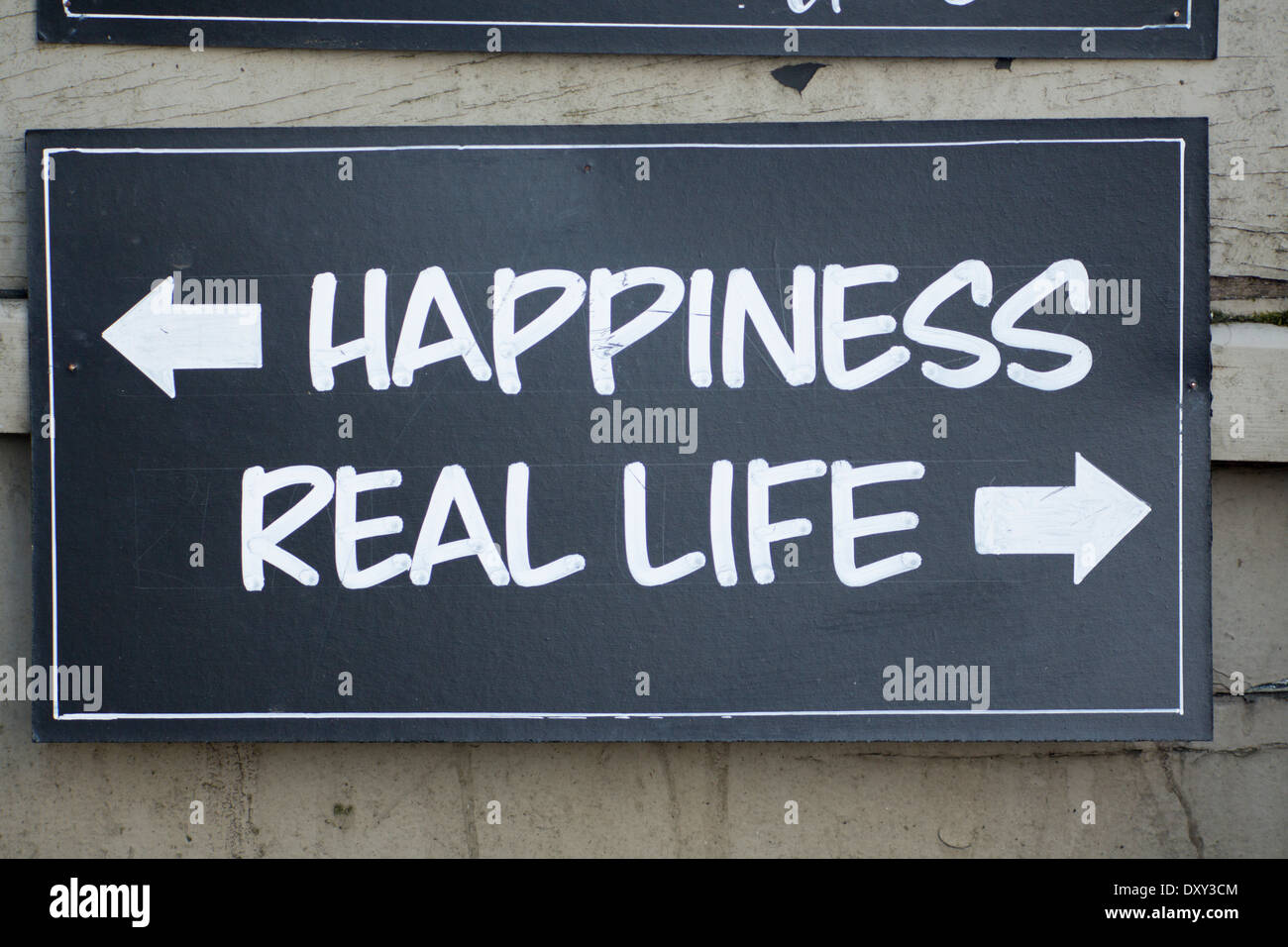 Blackboard sign with Happiness with arrow pointing in one direction and 'Real Life' with arrow pointing the other Escapism Stock Photo