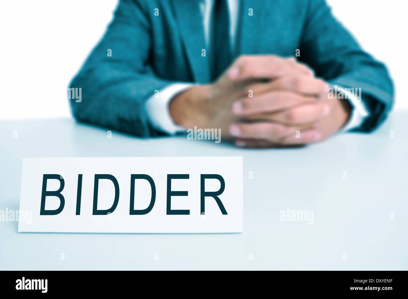 a man wearing a suit sitting in a desk with a desktop nameplate in front of him with the word bidder Stock Photo