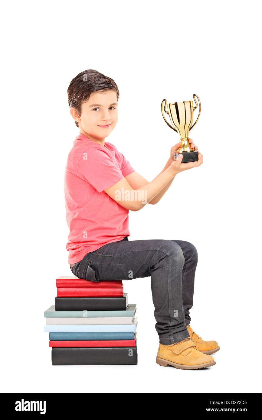 Little boy holding trophy seated on stack of books Stock Photo