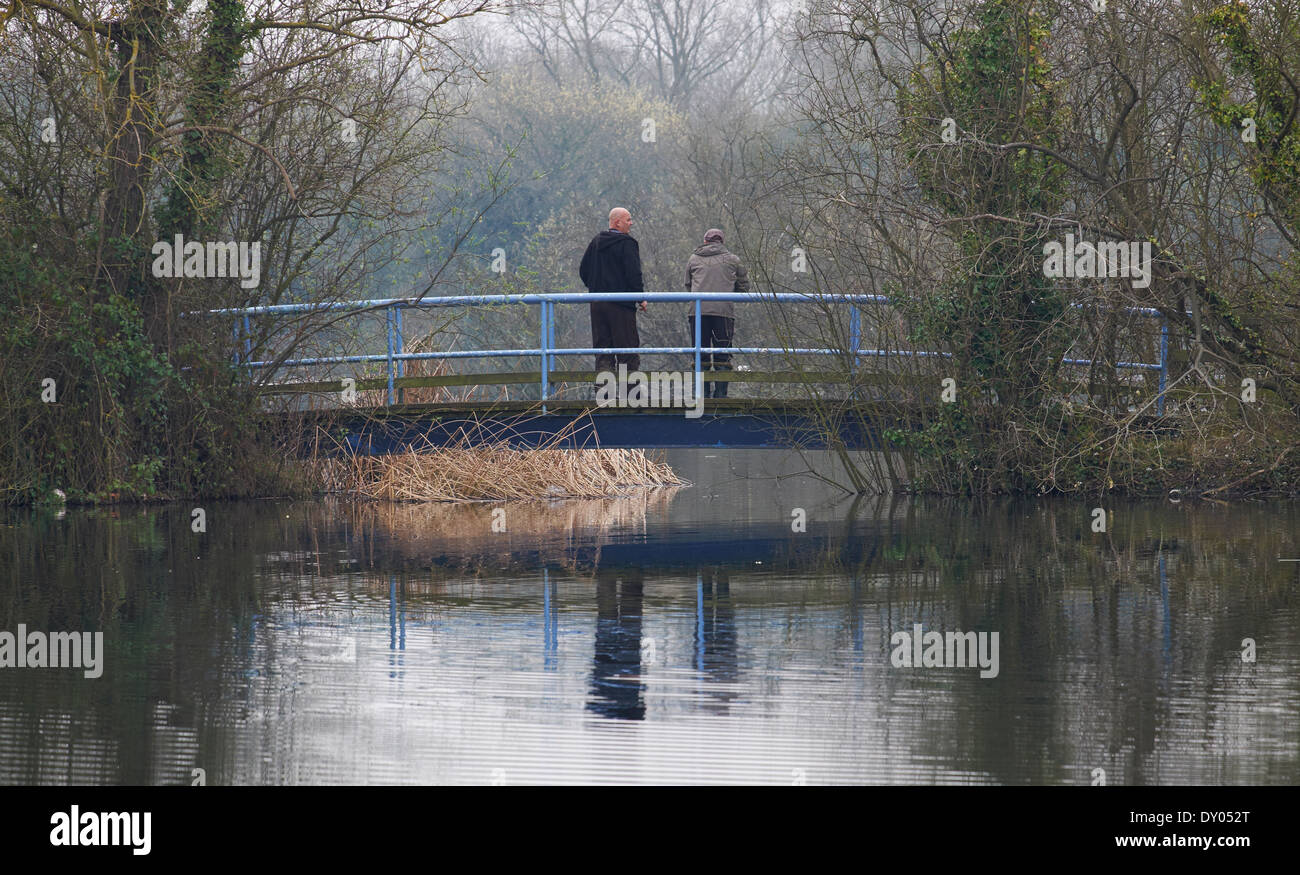 Two men on bridge over lake Milton Cambridgeshire England Stock Photo