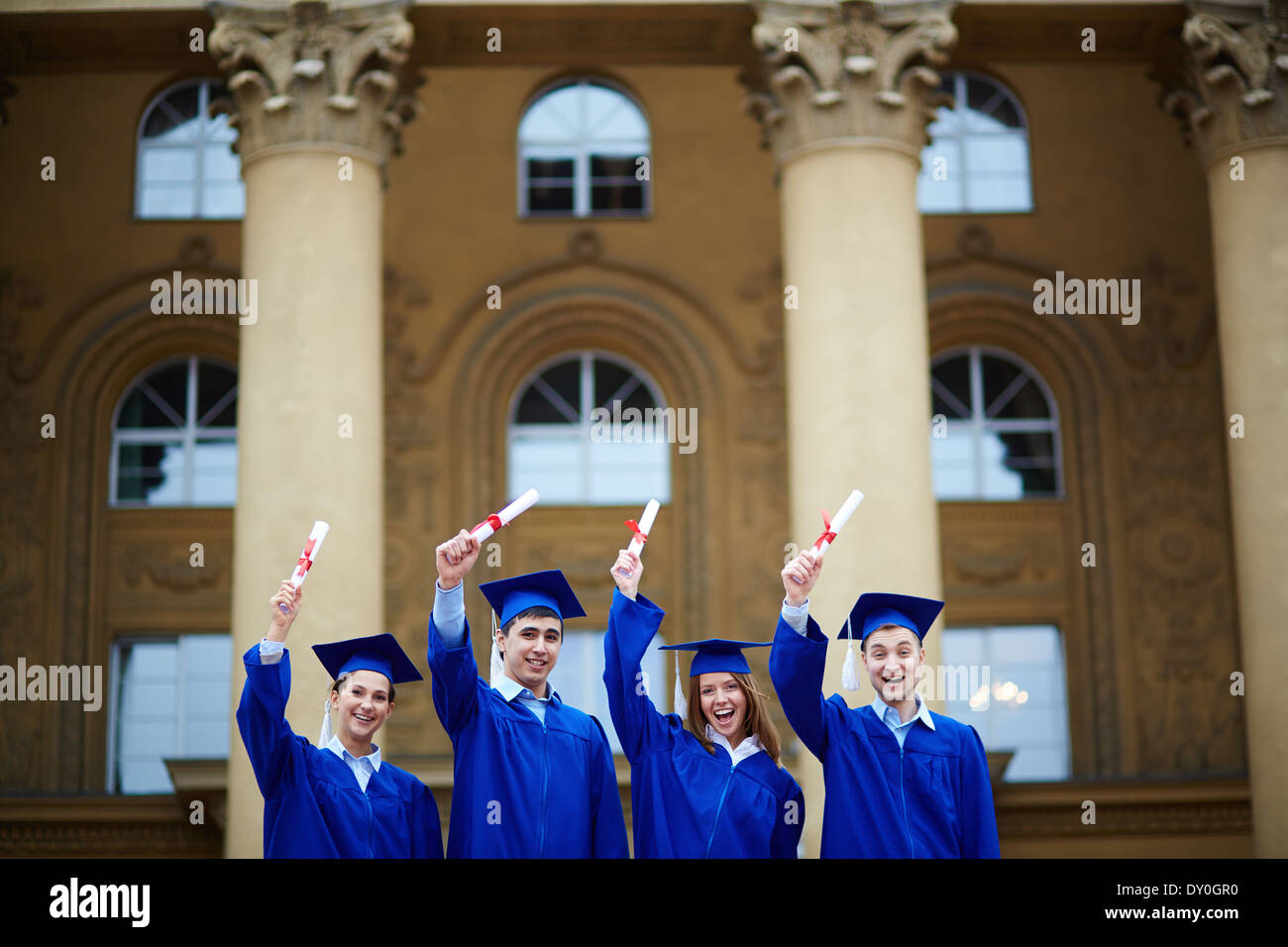 Group of cheerful students in graduation gowns showing their ...