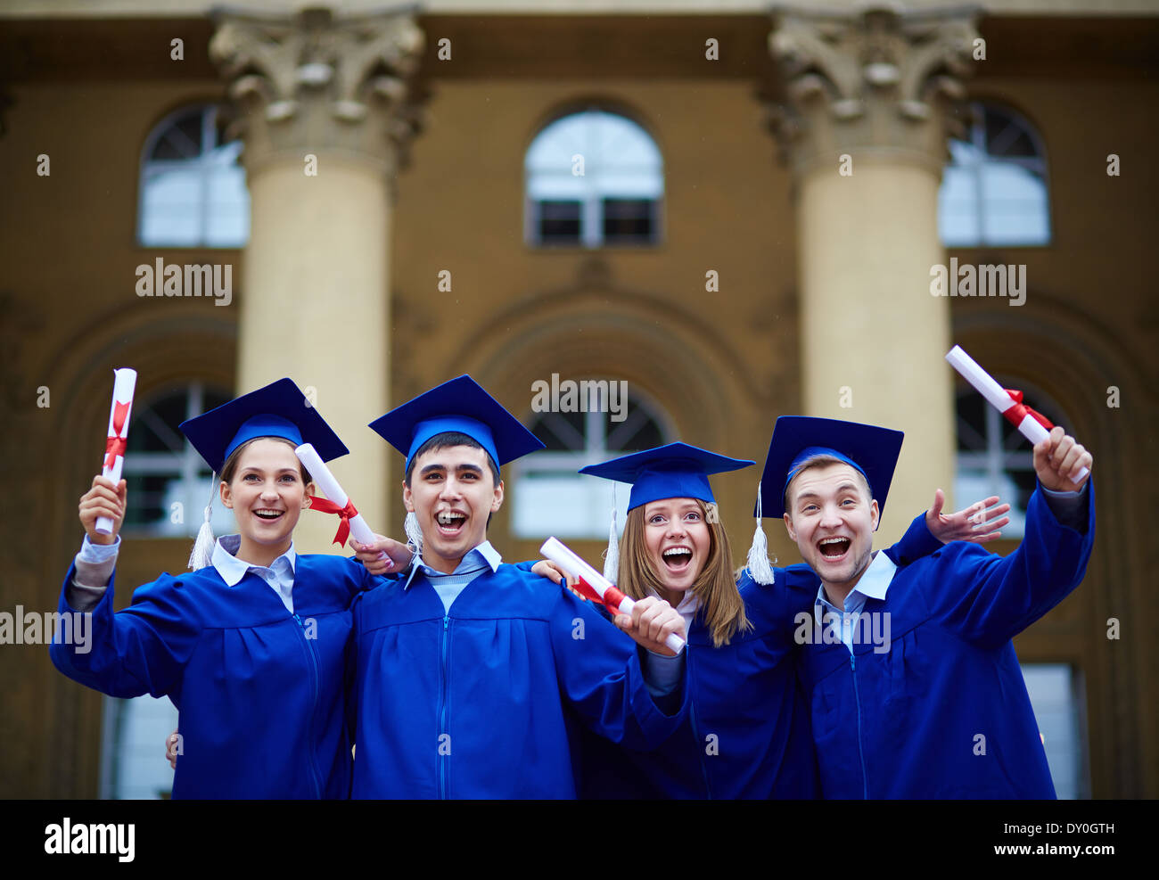 Group of smart students in graduation gowns holding diplomas Stock Photo