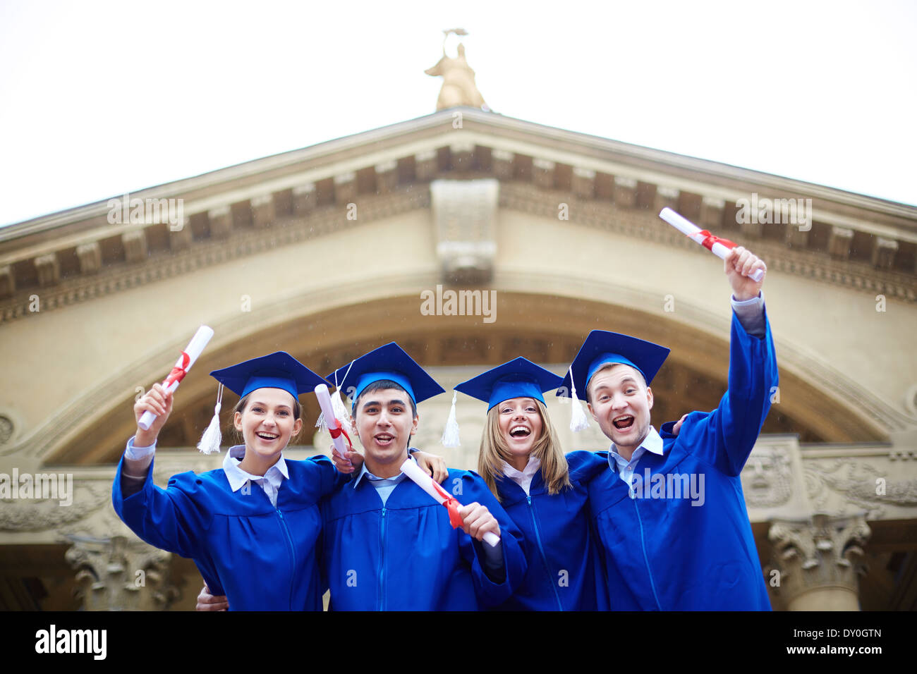 Group of ecstatic students in graduation gowns holding diplomas Stock Photo