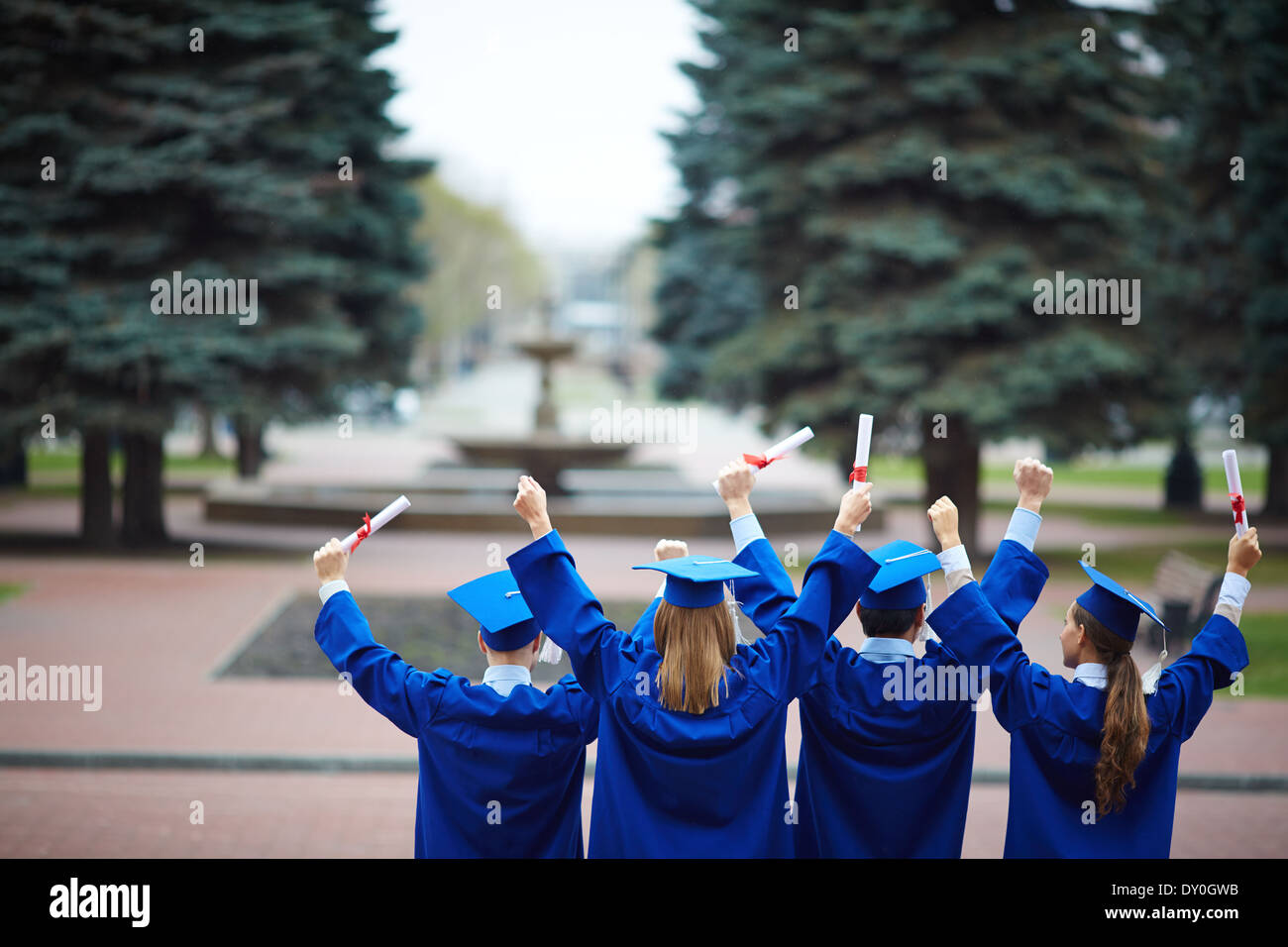 Backs of ecstatic students in graduation gowns holding diplomas Stock Photo