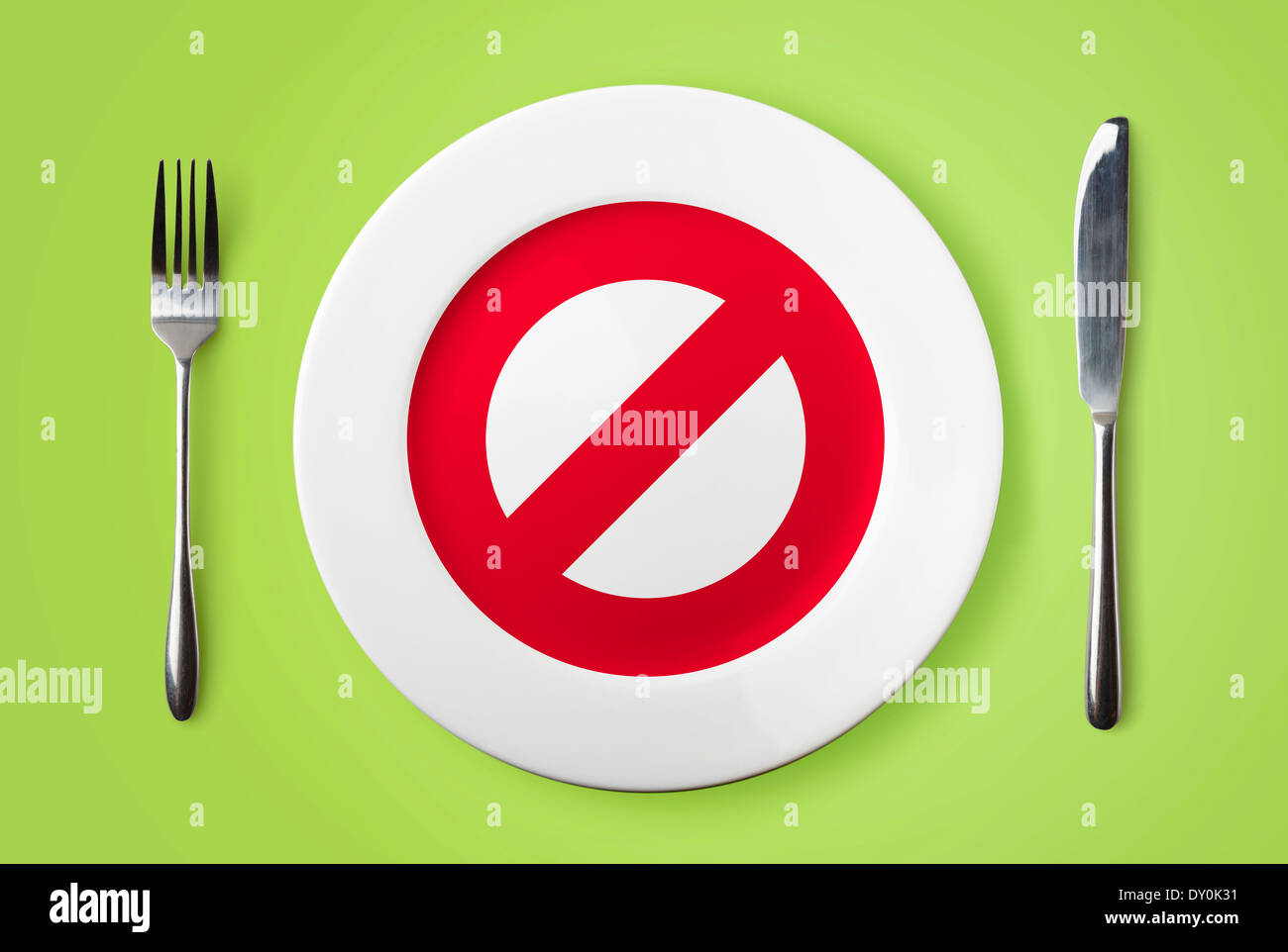 Empty plate with no red sign, fork and knife on green background Stock Photo