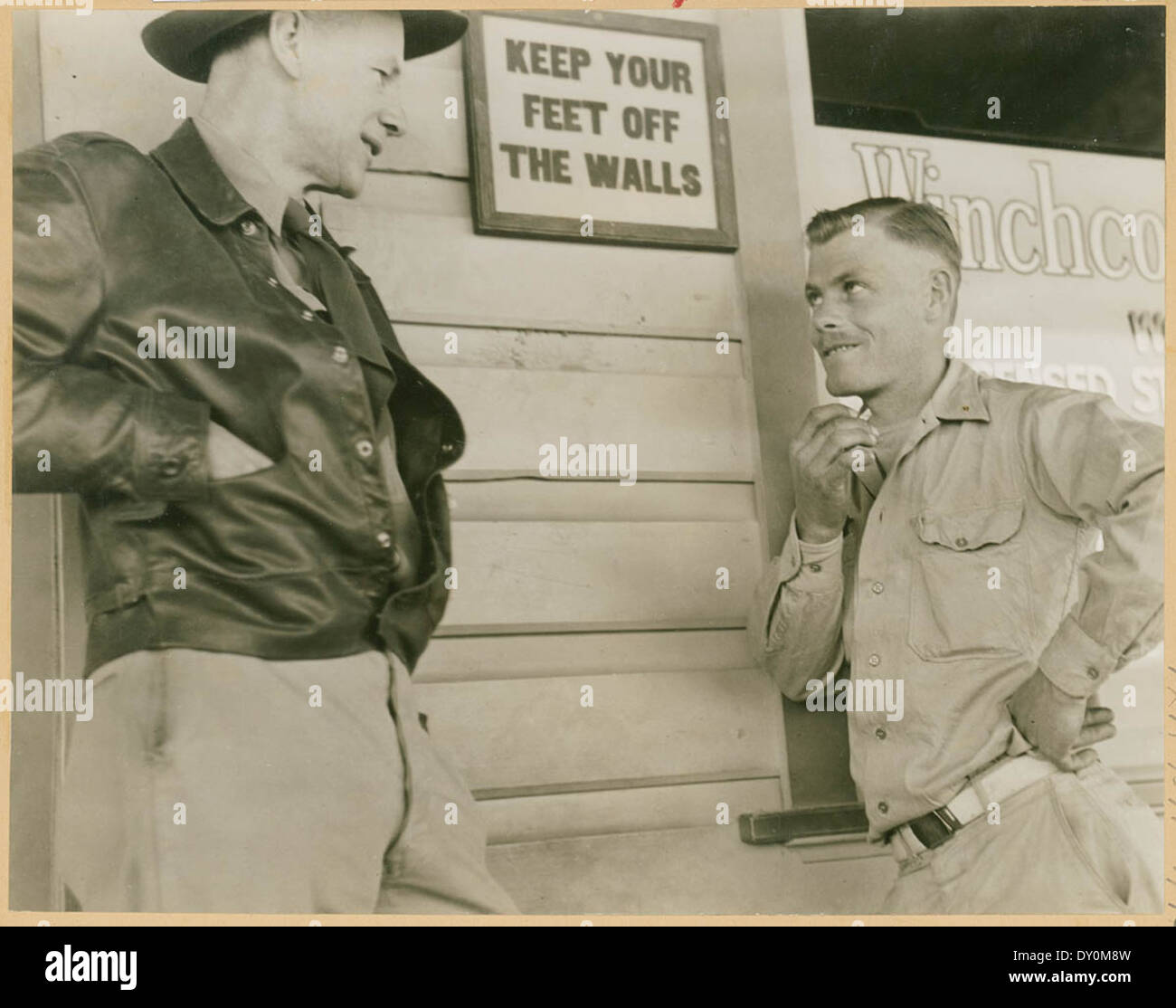 Two men talk next to sign: 'Keep your feet off the walls', Bourke, 1947, by L.Le Guay Stock Photo