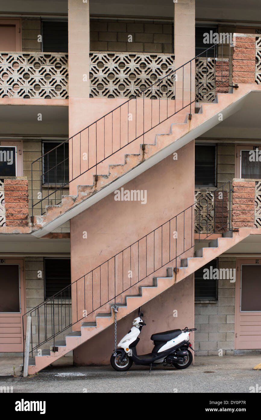 A motor scooter sits under a staircase leading up a residential building; Honolulu, Oahu, Hawaii, United States of America Stock Photo
