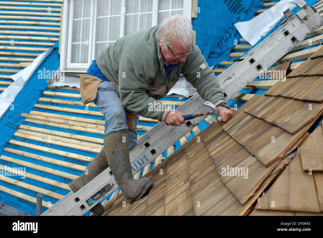 Home improvements - a roofer replaces a roof with cedar shingles, a thermally efficient, ecologically friendly material. Stock Photo