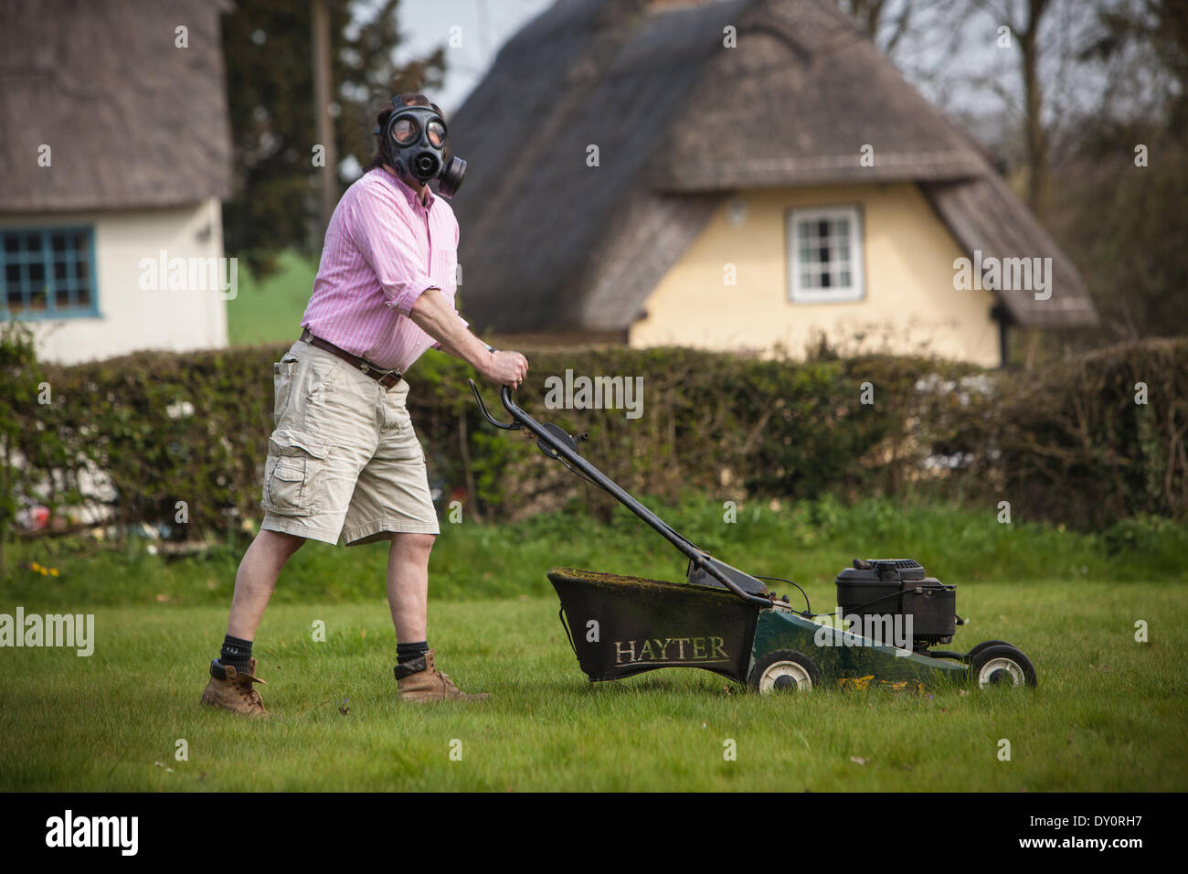 Arkesden, Essex . Man mowing the lawn wearing a gas mask as a