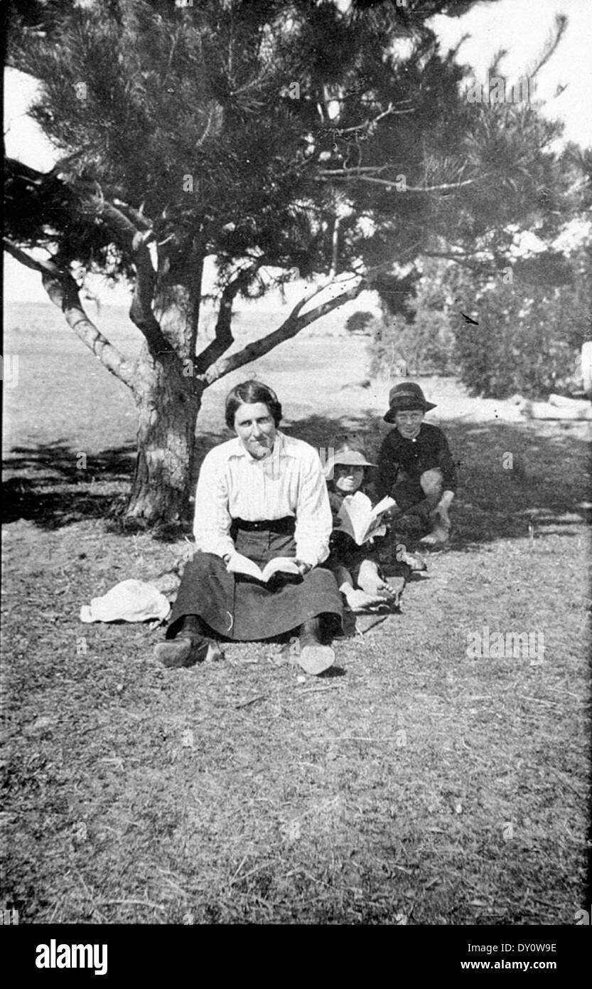 Reading outside under the pine tree with big sister on 'Balowra East' - Murringo, NSW, Photographed by - Jack English. Lottie English, Perce English, Bill English, c.1918 Stock Photo