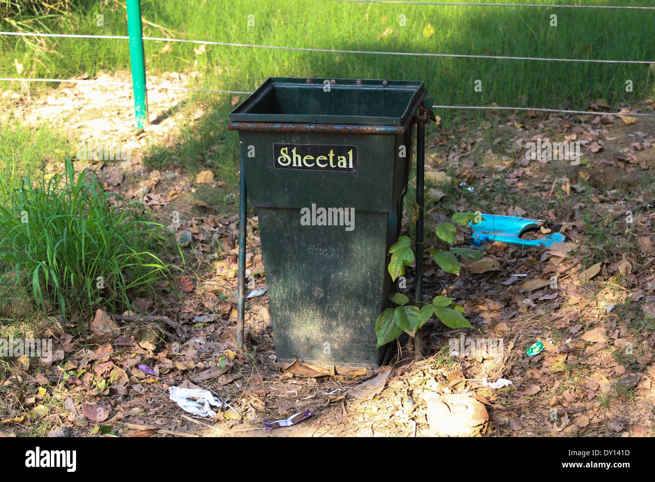 A rubbish bin inside the Delhi zoo, nestled among old leaves, with some grass nearby and some wire fences at the back Stock Photo