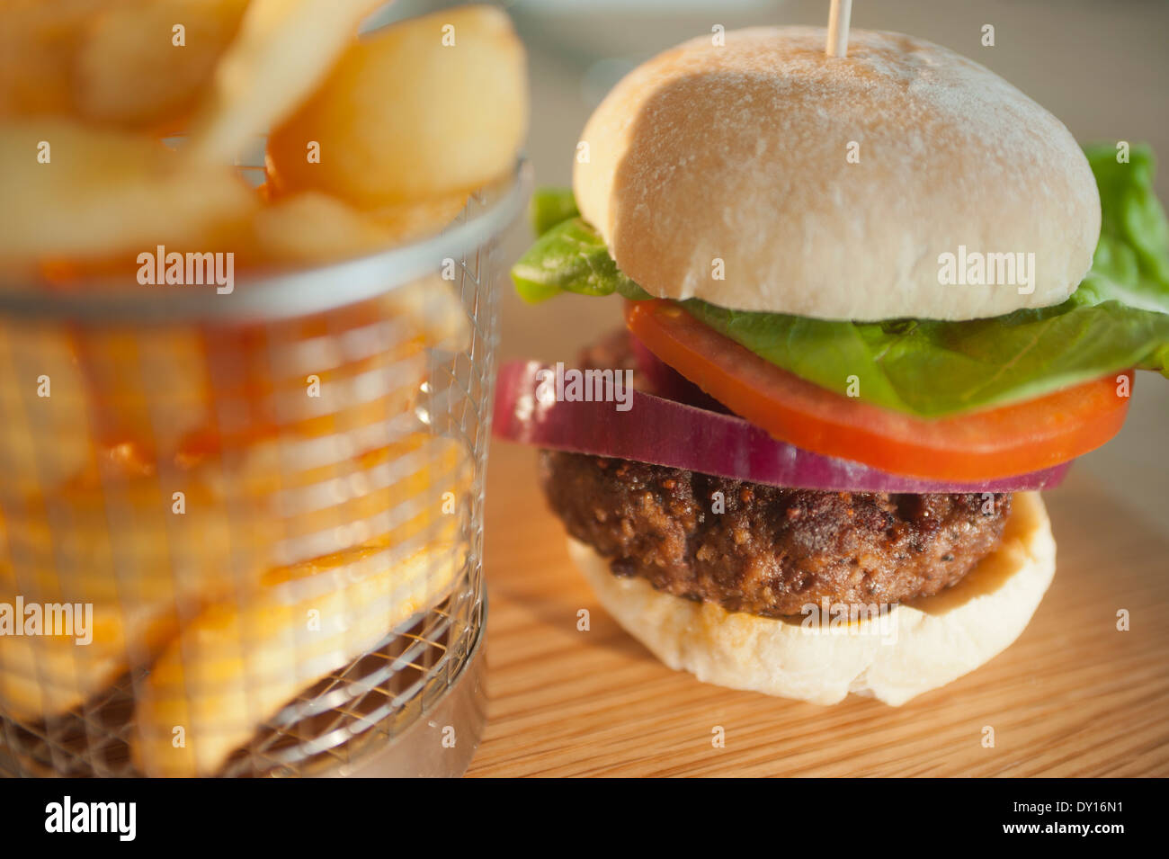 Classic burger with onion tomato and lettuce in a white bread bun with a side order of chips or French fried potatoes. Stock Photo