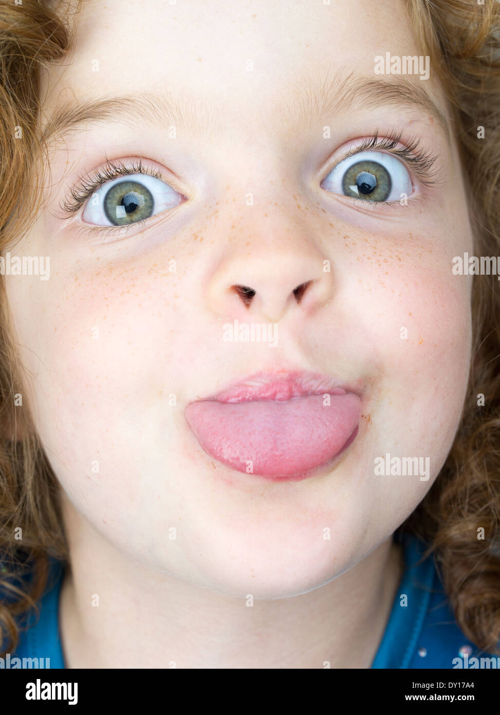 Young girl with red hair and big eyes sticking out her tongue Stock Photo