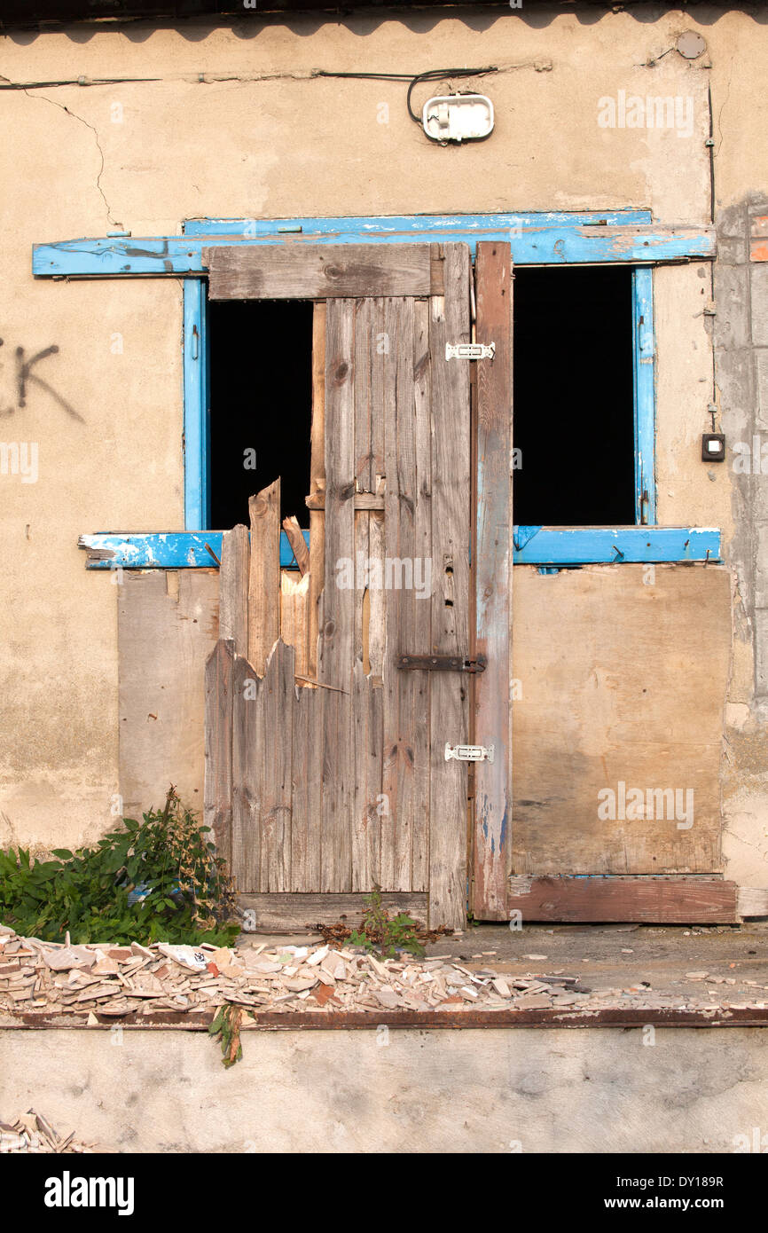 Dilapidated building with empty blue framed window and partial door frame leaning against it. Rzeczyca Central Poland Stock Photo