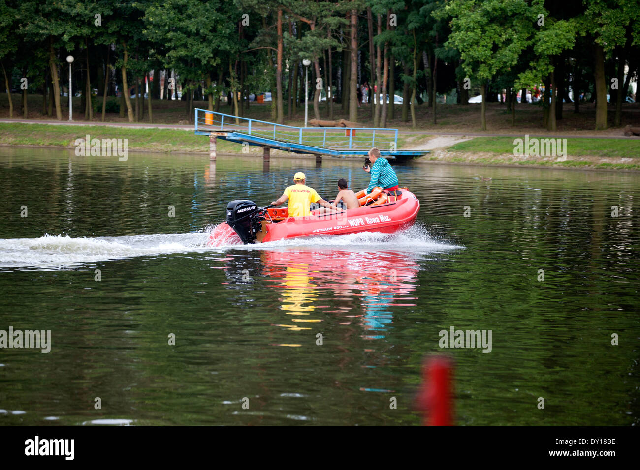 Lifeguard transporting kids in a motorized boat on Zalew Tatar lagoon to the waterfront park. Rawa Mazowiecka Central Poland Stock Photo