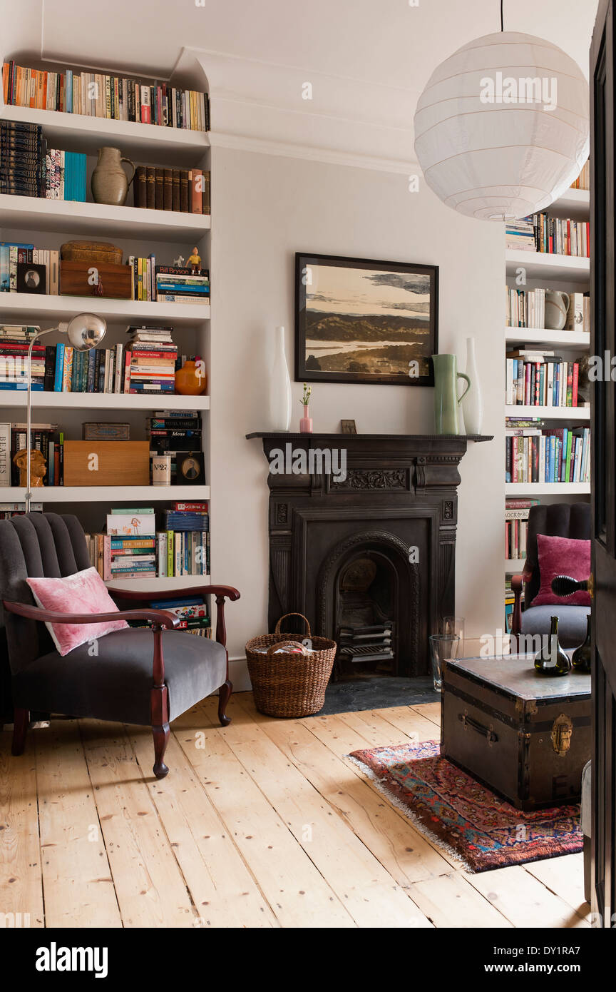 White-painted bookshelves in sitting room with traditional fireplace, old school trunk and grey armchair Stock Photo