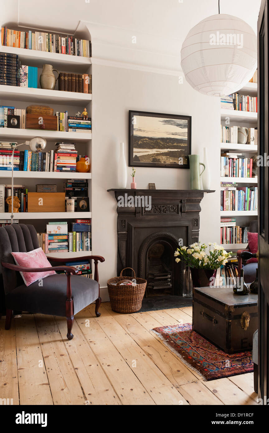 White-painted bookshelves in sitting room with traditional fireplace, old school trunk and grey armchair Stock Photo