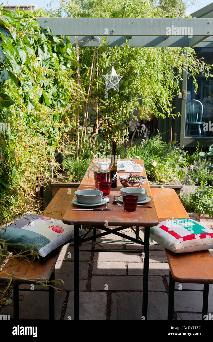 Wooden bench and table on paved garden patio underneath wooden pergola with cushions by Cassandra Ellis Stock Photo