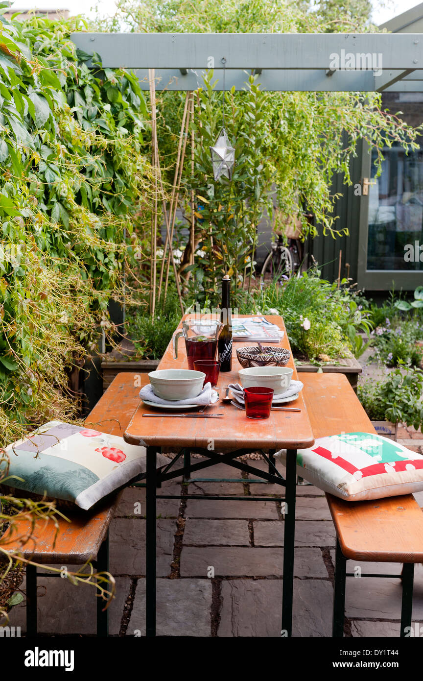 Wooden bench and table on paved garden patio underneath wooden pergola with cushions by Cassandra Ellis Stock Photo