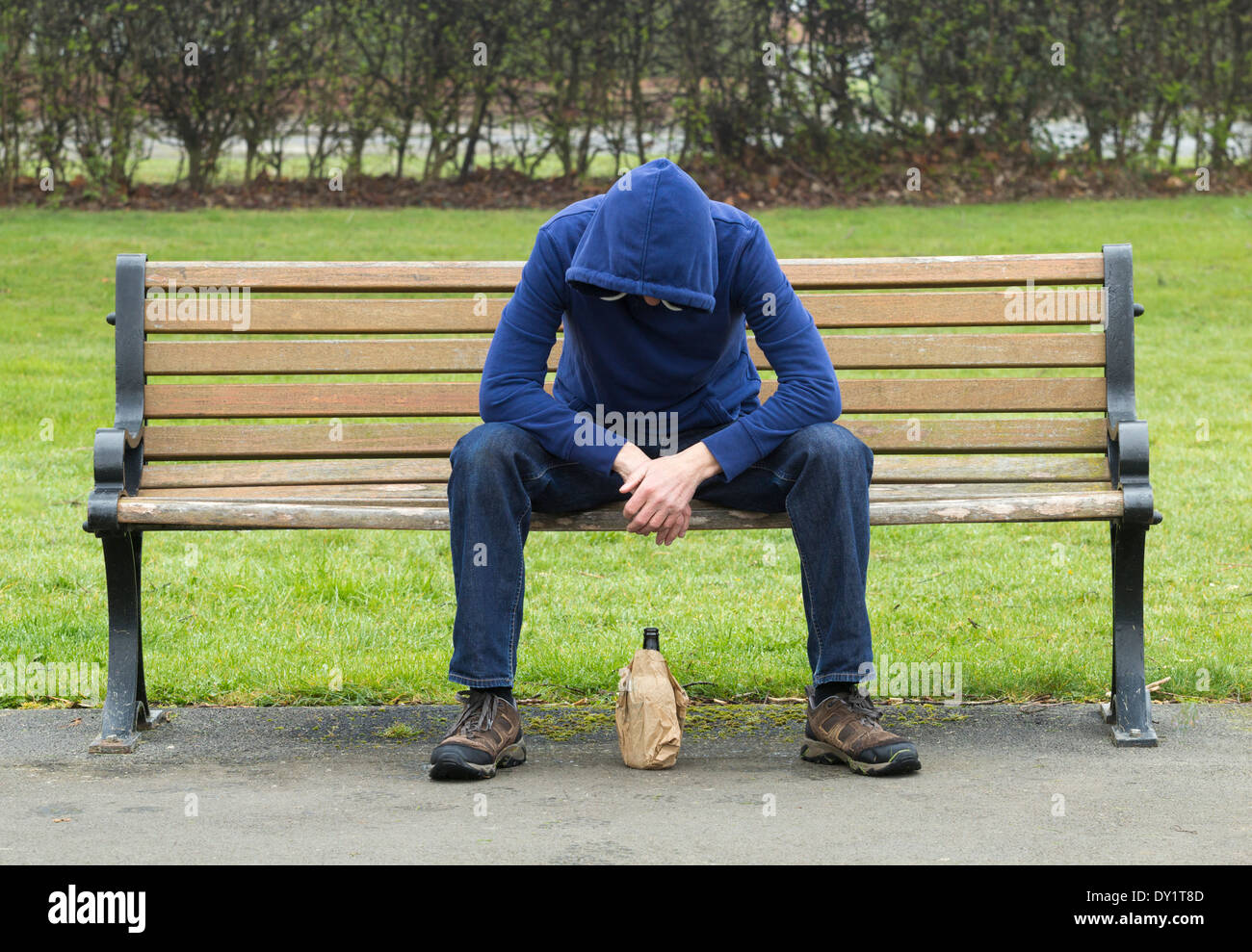 Male wearing hoodie sitting on park bench drinking alcohol Stock Photo