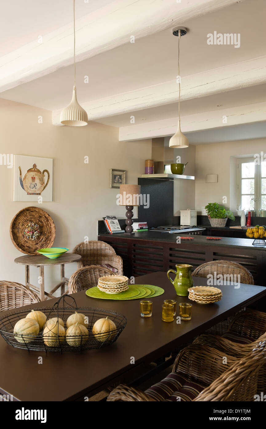 Cane chairs around a coated metal dining table in a kitchen with traditional beamed ceiling, Lacanche cooker and wire bowls Stock Photo