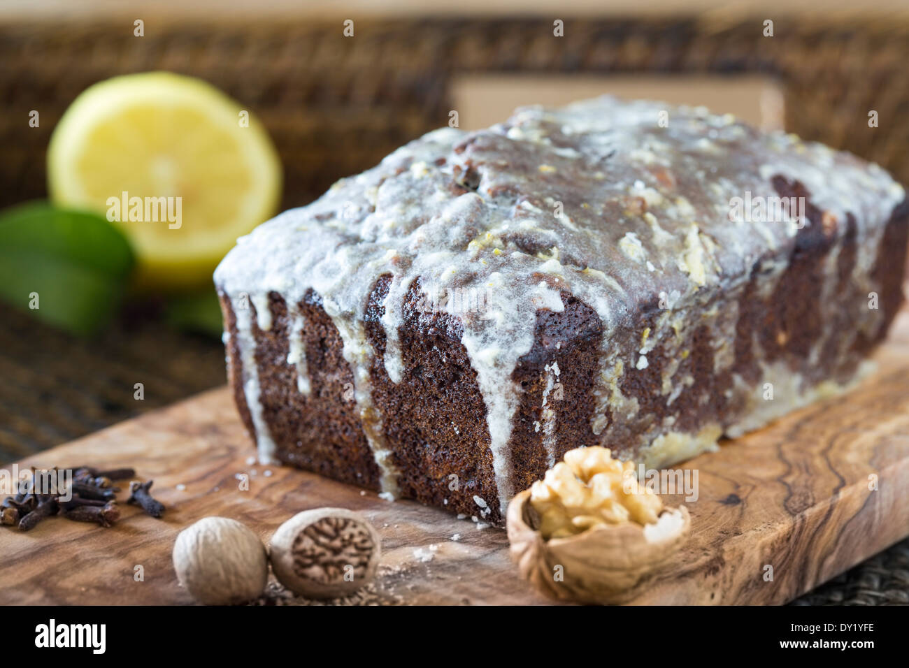 Whole iced homemade date and walnut cake on wooden board and woven tray. Stock Photo