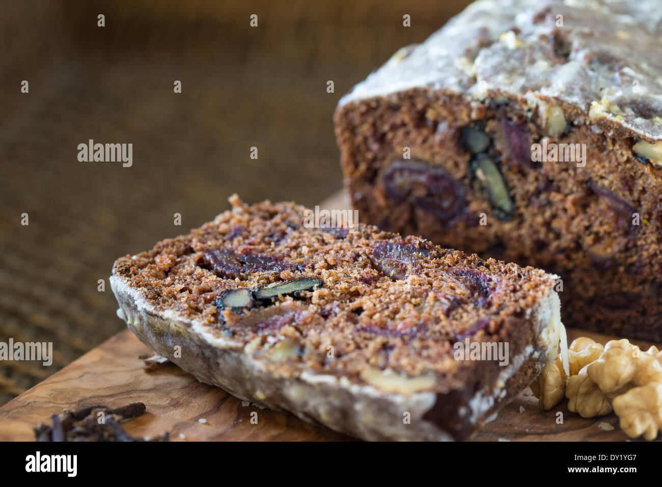 Sliced homemade date and walnut cake on wooden board and woven tray. Stock Photo