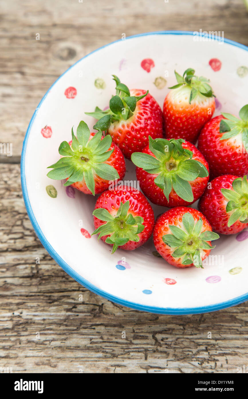 Whole Spanish strawberries in a ceramic rustic bowl, placed on rustic wooden table Stock Photo