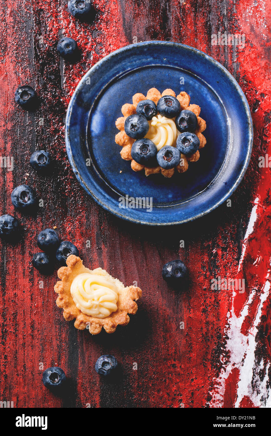 Top view on blueberry mini tarts served on blue ceramic plate over black and red wooden background. Stock Photo