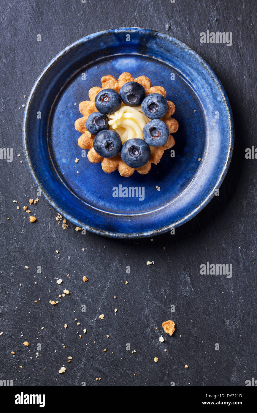 Top view on blueberry mini tart served on blue ceramic plate over dark stone background. Stock Photo