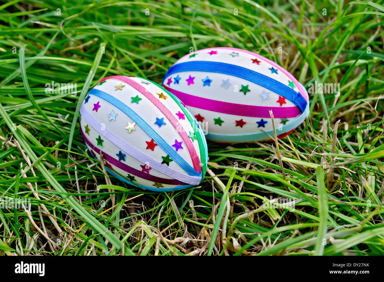 Two easter eggs, decorated with multicolored braid and sparkles as asterisks on the green grass Stock Photo