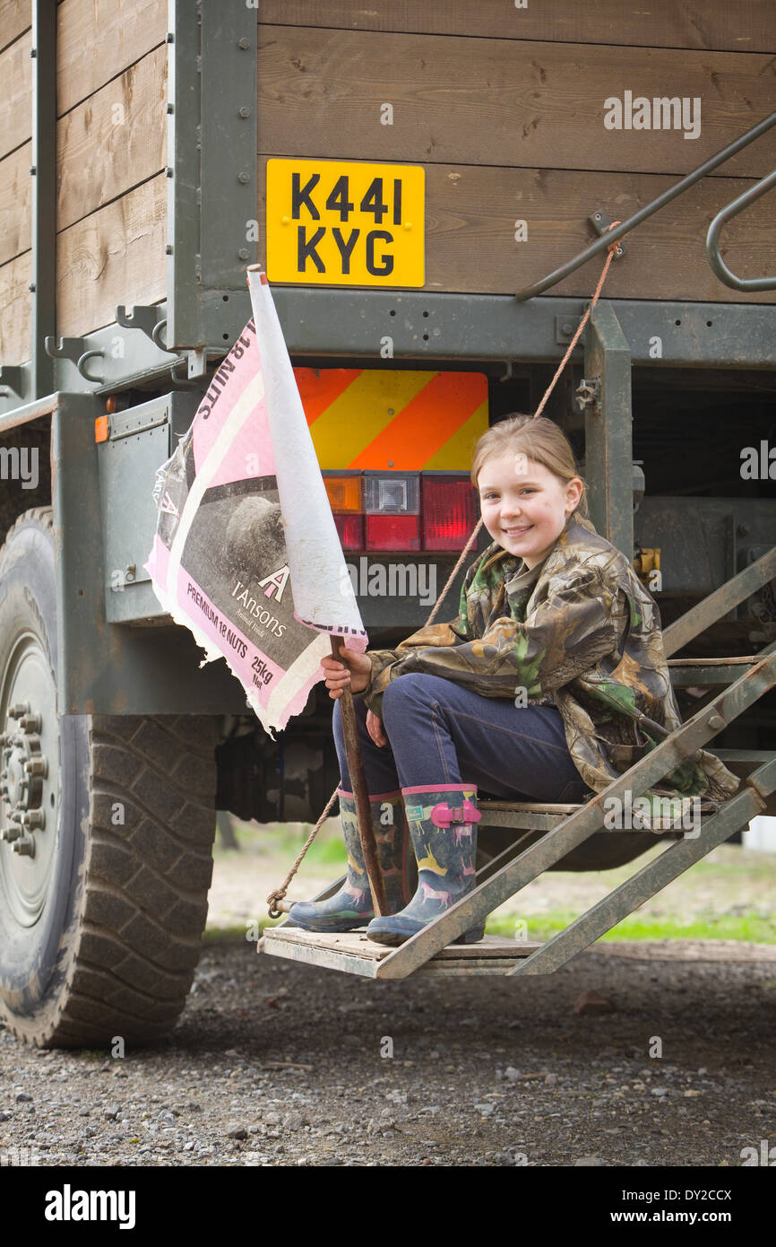 A young girl bush beater holding a home made flag while sitting on the back of a beaters or guns truck on a shoot Stock Photo